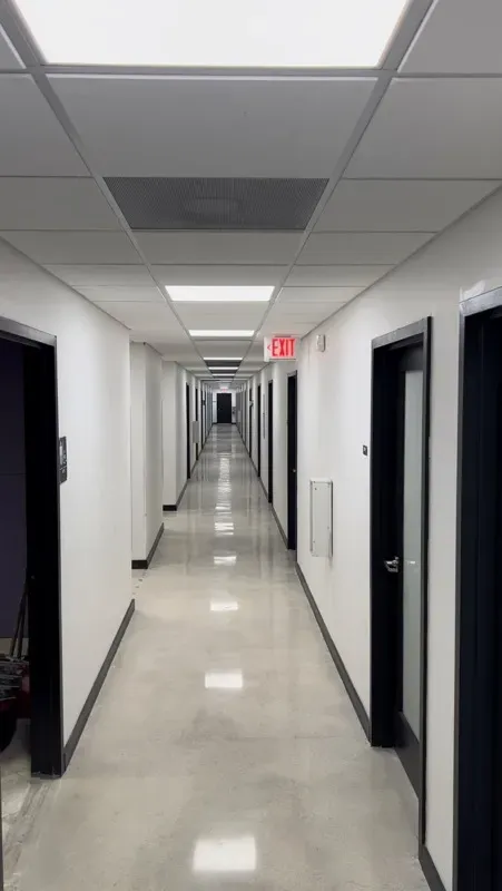 Long office corridor with a light, high-gloss seamless resin floor reflecting the ceiling lights