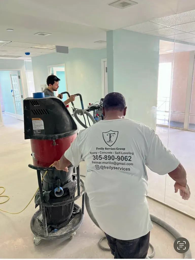 Two Freily technicians in branded shirts running a floor grinder inside a bright interior