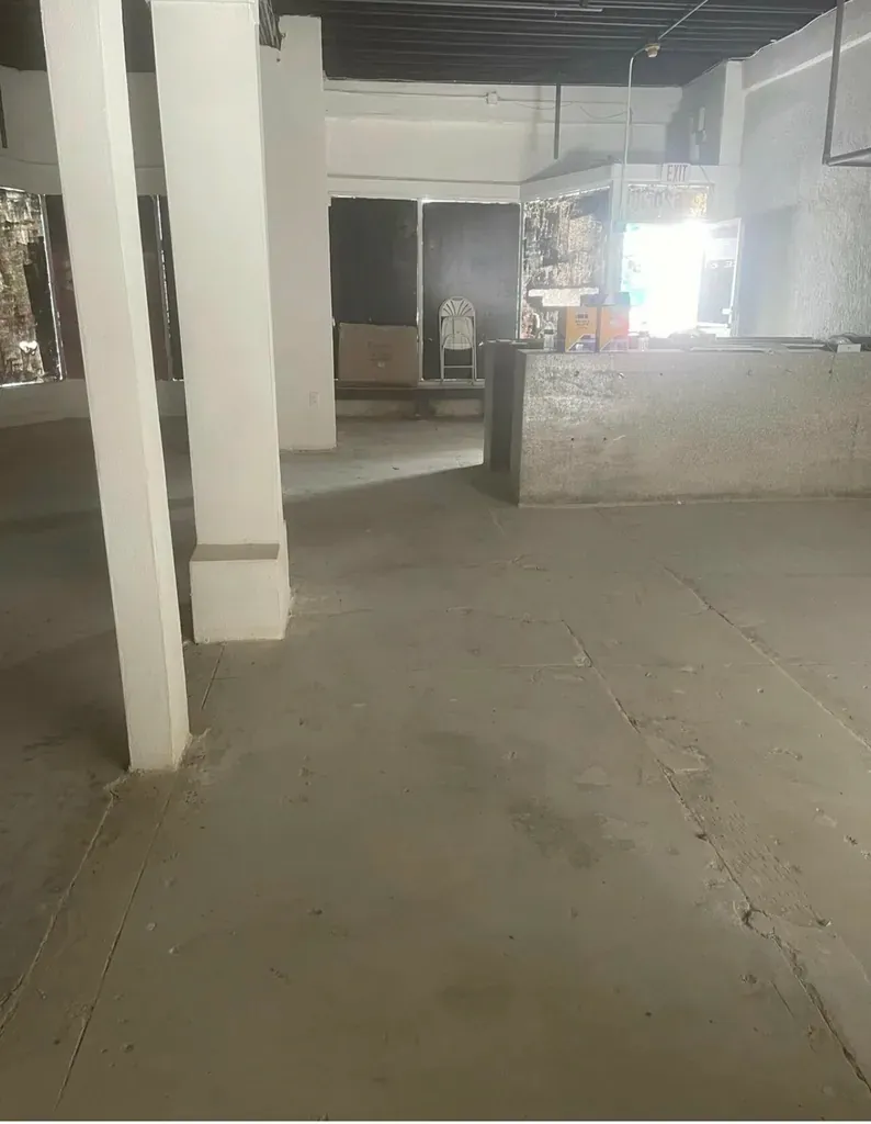 Empty commercial space under renovation with exposed concrete floor and support columns